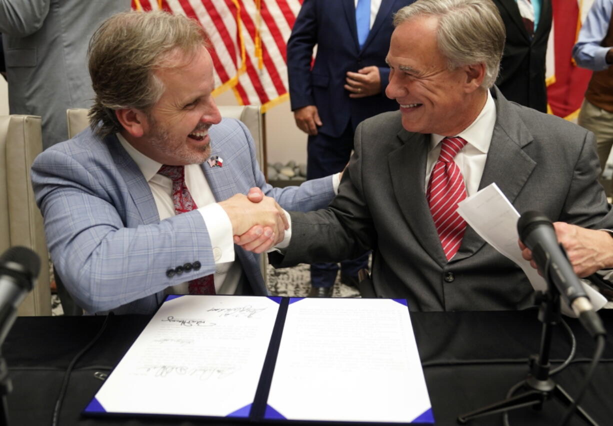 Texas Gov. Greg Abbott, right, and state Sen. Bryan Hughes, R-Mineola, shake hands after Abbott signed Senate Bill 1, also known as the Election Integrity Bill, on Tuesday in Tyler, Texas. The measure further tightens the state's strict voting laws.