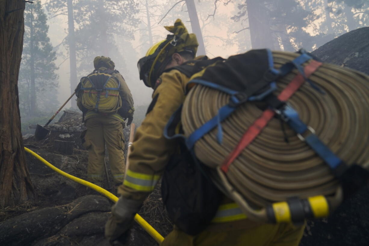 Two firefighters from Cosumnes Fire Department carry water hoses while holding a fire line to keep the Caldor Fire from spreading in South Lake Tahoe, Calif., Friday, Sept. 3, 2021. Fire crews took advantage of decreasing winds to battle a California wildfire near popular Lake Tahoe and were even able to allow some people back to their homes but dry weather and a weekend warming trend meant the battle was far from over. (AP Photo/Jae C.