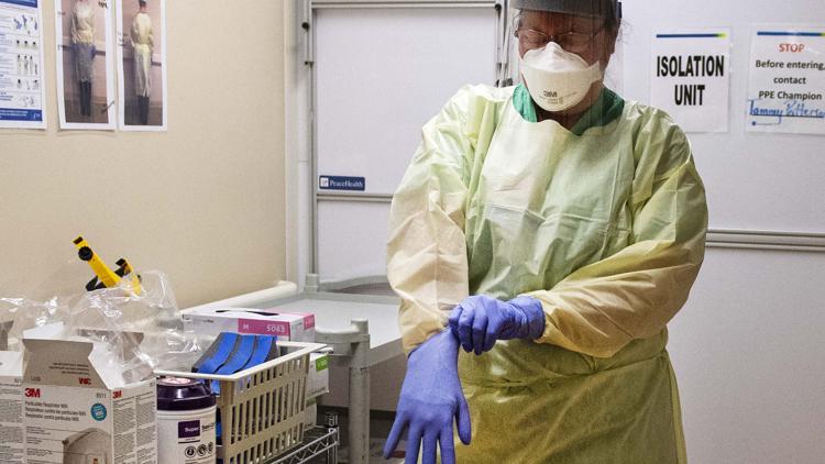 In March, PeaceHealth St. John Medical Center nurse Tammy Patterson puts on gloves in preparation to enter the hospital's isolation unit  where COVID-19 patients are treated.