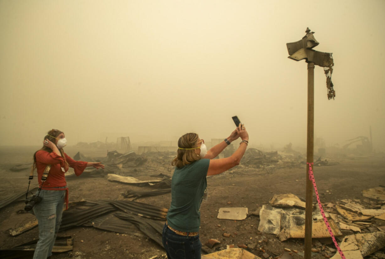 Kelly Tan, 59, left, looks on as her sister, Tiffany Lozano, 44, photographs melted street signs on Main St. in Greenville, California, caused by the extreme temperature of the Dixie Fire that destroyed most of the town. Lozano is a resident of nearby Quincy and Tan is a resident of nearby Taylorsville.