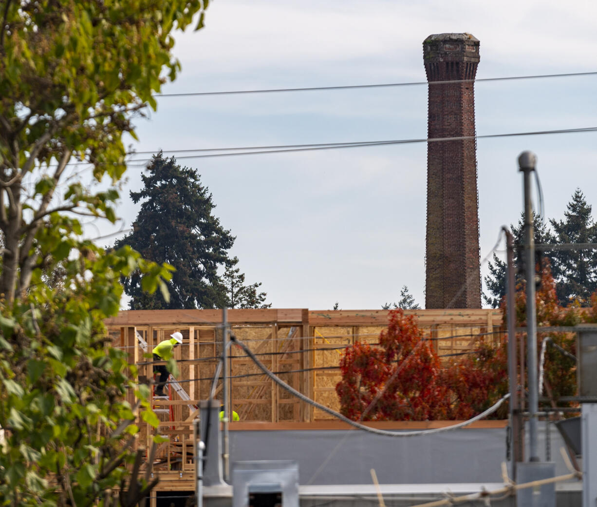 Construction workers continue building an apartment building Tuesday, Oct. 19, 2021, as the Providence Academy smokestack stands in the distance. The Vancouver City Council decided Monday to uphold a demolition permit for Providence AcademyÄôs landmark smokestack.