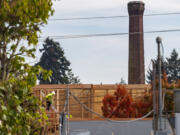 Construction workers continue building an apartment building Tuesday, Oct. 19, 2021, as the Providence Academy smokestack stands in the distance. The Vancouver City Council decided Monday to uphold a demolition permit for Providence AcademyÄôs landmark smokestack.