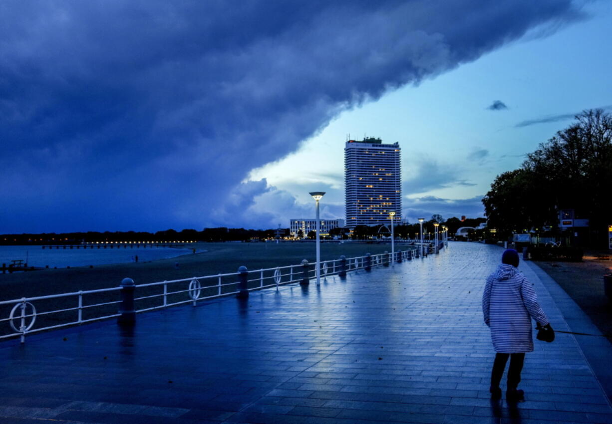 A woman walks on the promenade at the Baltic Sea in Travemuende, northern Germany, Thursday, Oct.21, 2021. Northern Germany was hit by storm and heavy rain falls.