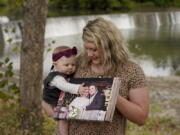 Aubrea Baker holds her wedding photo as she and her 7-month-old daughter, Haylen, visit one of her late husband's favorite fishing spots Saturday in Burlington, Kan. Her husband, Danny Baker, is among the more than 700,000 U.S.