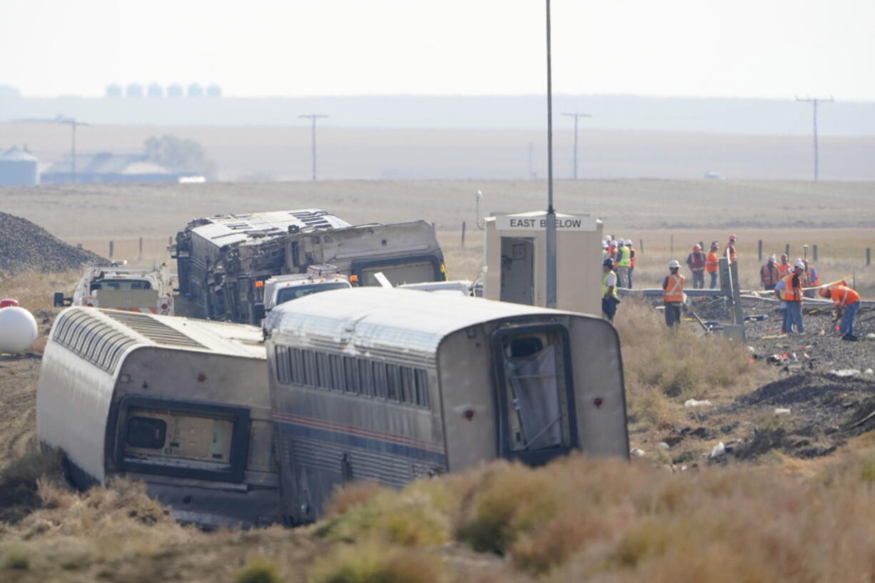 Workers stand near train tracks, Monday, Sept. 27, 2021, next to overturned cars from an Amtrak train that derailed Saturday, near Joplin, Mont., killing three people and injuring others. Federal investigators are seeking the cause of the derailment. (AP Photo/Ted S.