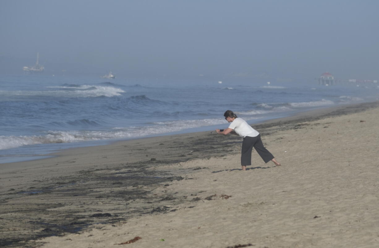 A woman takes a picture of oil washed up on Huntington Beach, Calif., Sunday., Oct. 3, 2021. A major oil spill off the coast of Southern California fouled popular beaches and killed wildlife while crews scrambled Sunday to contain the crude before it spread further into protected wetlands. (AP Photo/Ringo H.W.