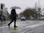 A pedestrian carries an umbrella while crossing a street at Fisherman's Wharf in San Francisco, Wednesday, Oct. 20, 2021. Showers drifted across the drought-stricken and fire-scarred landscape of Northern California on Wednesday, trailed by a series of progressively stronger storms that are expected to bring significant rain and snow into next week, forecasters said.