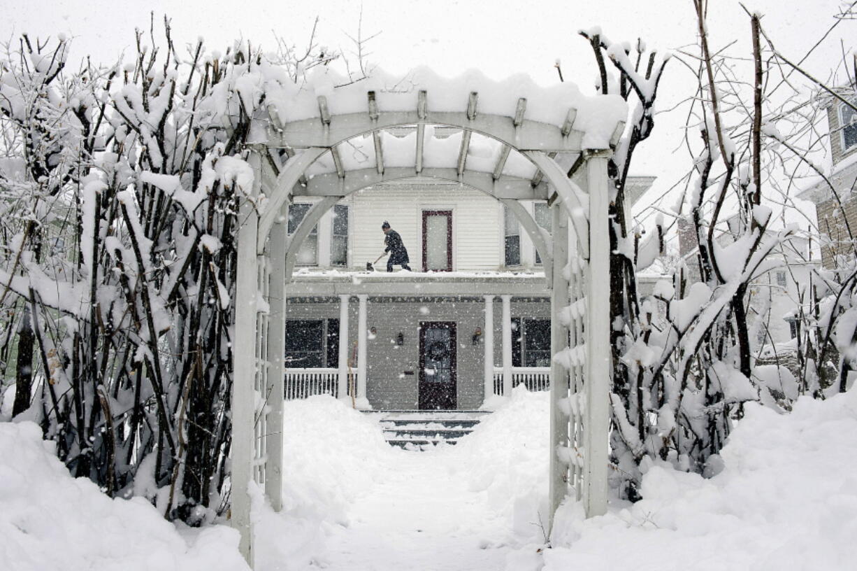 FILE - Amber Cox shovels snow from the porch roof at her home in Auburn, Maine, on March 8, 2018.  With prices surging worldwide for heating oil, natural gas and other fuels, the U.S. government said Wednesday, Oct. 13, 2021 it expects households to see jumps of up to 54% for their heating bills compared to last winter.