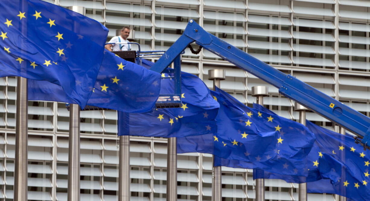 FILE- In this June 23, 2016 file photo, a worker on a lift adjusts the EU flags in front of EU headquarters in Brussels. The European Union's enlargement policy is at an impasse as its leaders gather for a summit focused on how to deal with Western Balkans neighbors that have been trying to enter the club for two decades.