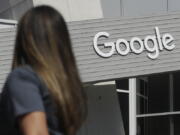 FILE - In this Sept. 24, 2019, file photo, a woman walks below a Google sign on the campus in Mountain View, Calif.  Google on Thursday, Oct. 7, 2021, will no longer allow digital ads promoting false climate change claims to appear next to the content of other publishers, hoping to deny money to those making such claims and to stop the spread of misinformation on its platform.