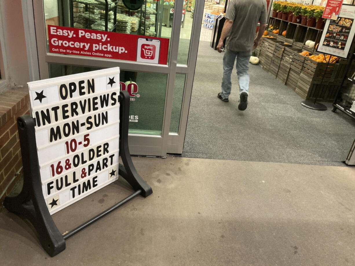 In this Thursday, Oct. 7, 2021, photograph, a sign for potential hires stands outside the door to a Hy-Vee grocery store in Sioux Falls, S.D. Companies that typically hire thousands of seasonal workers are heading into the holidays during one of the tightest job markets in decades, making it unlikely they'll find all the workers they need. For shoppers, it might mean a less than jolly holiday shopping experience, with bare store shelves and online orders that take longer than usual to fill.