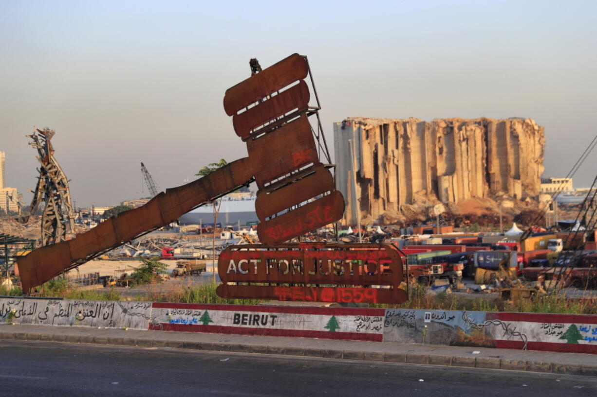 FILE - In this Aug. 4, 2021 file photo, a monument that represents justice stands in front of towering grain silos that were gutted in the massive August 2020 explosion at the port that killed more than 200 people and wounded over 6,000, in Beirut, Lebanon. For eight months Tarek Bitar, a relatively obscure judge has quietly investigated one of the world's worst non-nuclear explosions with only two assistants helping him -- and a lot of powerful detractors blocking him. For many Lebanese Bitar is their only hope for truth and accountability in a country that craves both. But for the country's entrenched political class, the 47-year-old Bitar has become a nightmare that needs to be dealt with.