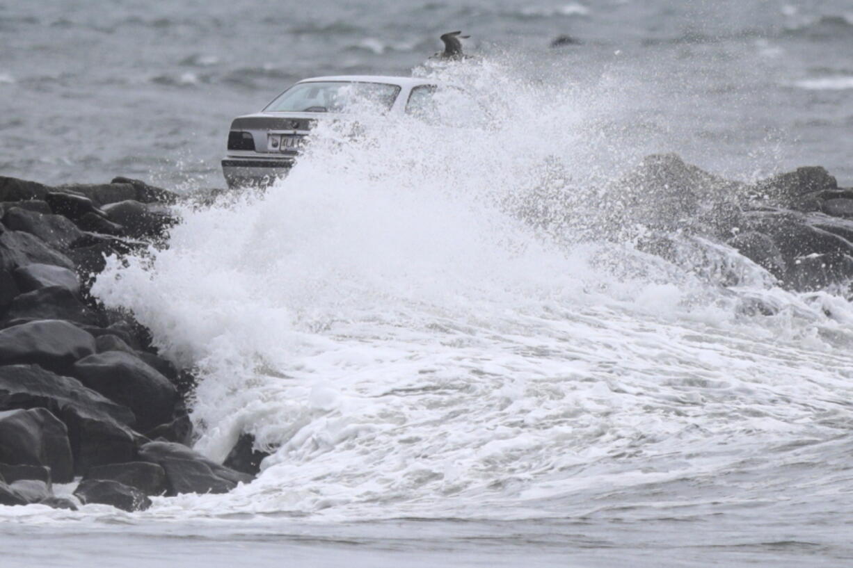 A car making its way across the Gooseberry Island causeway, Tuesday, Oct. 26, 2021, in Westport, Mass., is covered by a large wave, as a nor'easter makes its way across the northeast.