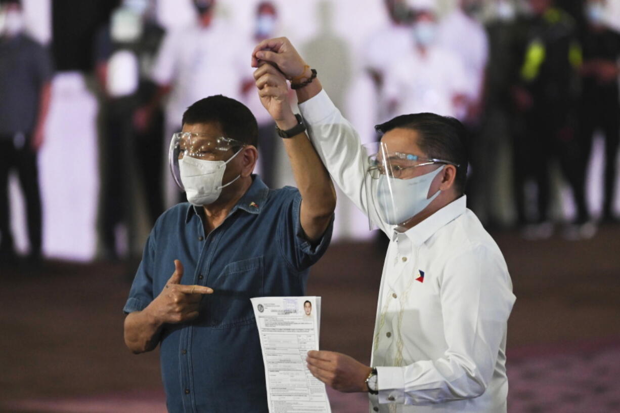 Philippine President Rodrigo Duterte, left, raises the hand of Sen. Bong Go who has filed his certificate of candidacy for vice-president during next year's elections before the Commission on Elections at the Sofitel Harbor Garden Tent in Metropolitan Manila, Philippines on Saturday, Oct. 2, 2021. Duterte says he is backing out of an announced plan to run for vice president in next year's elections and will retire from politics after his term ends.