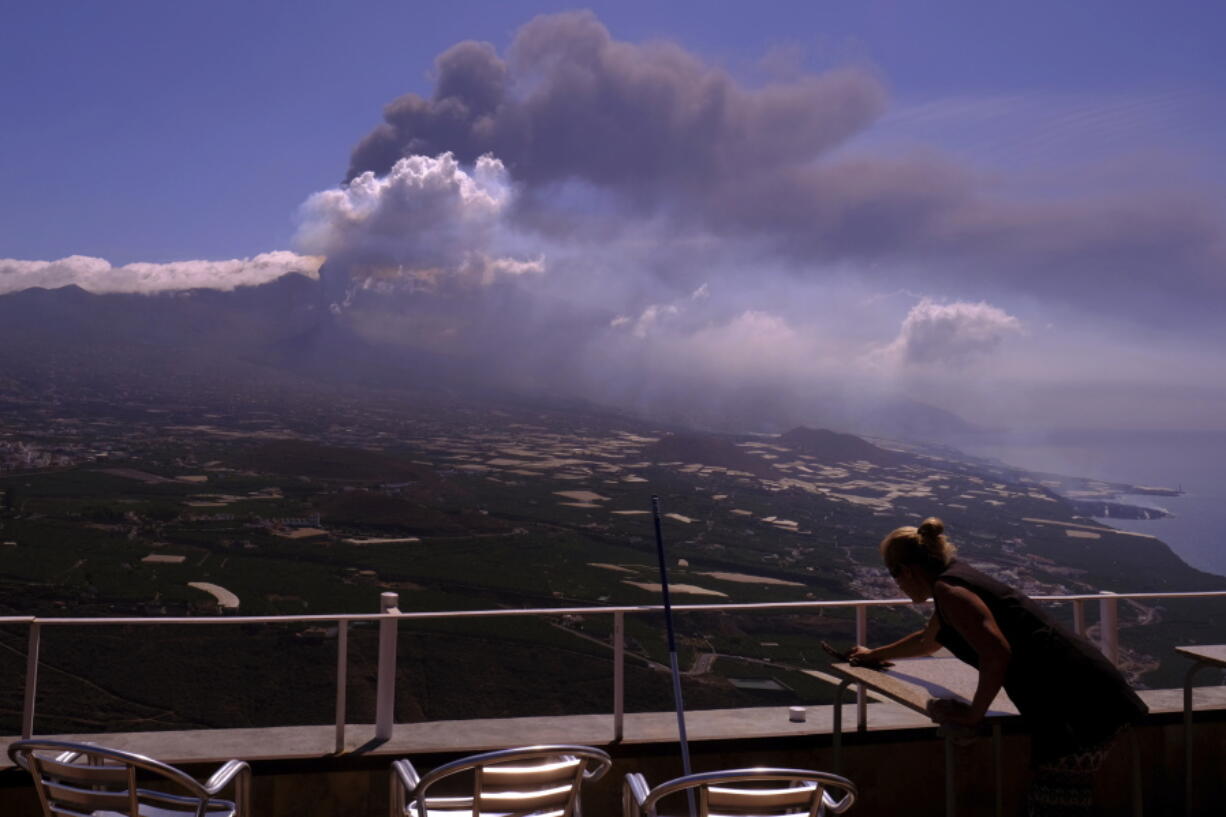 A worker cleans the ash from the tables of a restaurant as lava flows from a volcano on the Canary island of La Palma, Spain on Monday Oct. 4, 2021. More earthquakes are rattling the Spanish island of La Palma, as the lava flow from an erupting volcano surged after part of the crater collapsed. Officials say they don't expect to evacuate any more people from the area, because the fiery molten rock was following the same route to the sea as earlier flows.