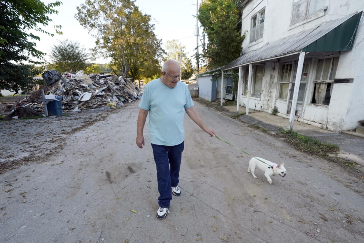 Tommy Goodwin walks his dog, Tasha, down a street lined with flood-damaged buildings and piles of debris Sept. 27, 2021, in Waverly, Tenn. After a devastating flood hit Aug. 21, the town of just over 4,000 people faces a dilemma. More than 500 homes and 50 businesses were damaged. That will likely result in massive revenue losses while the city spends millions on cleanup and repairs. If those homes and businesses don't return, the town could die a lingering death. But if they build back along the creek, they could be risking another disaster.