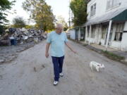 Tommy Goodwin walks his dog, Tasha, down a street lined with flood-damaged buildings and piles of debris Sept. 27, 2021, in Waverly, Tenn. After a devastating flood hit Aug. 21, the town of just over 4,000 people faces a dilemma. More than 500 homes and 50 businesses were damaged. That will likely result in massive revenue losses while the city spends millions on cleanup and repairs. If those homes and businesses don't return, the town could die a lingering death. But if they build back along the creek, they could be risking another disaster.