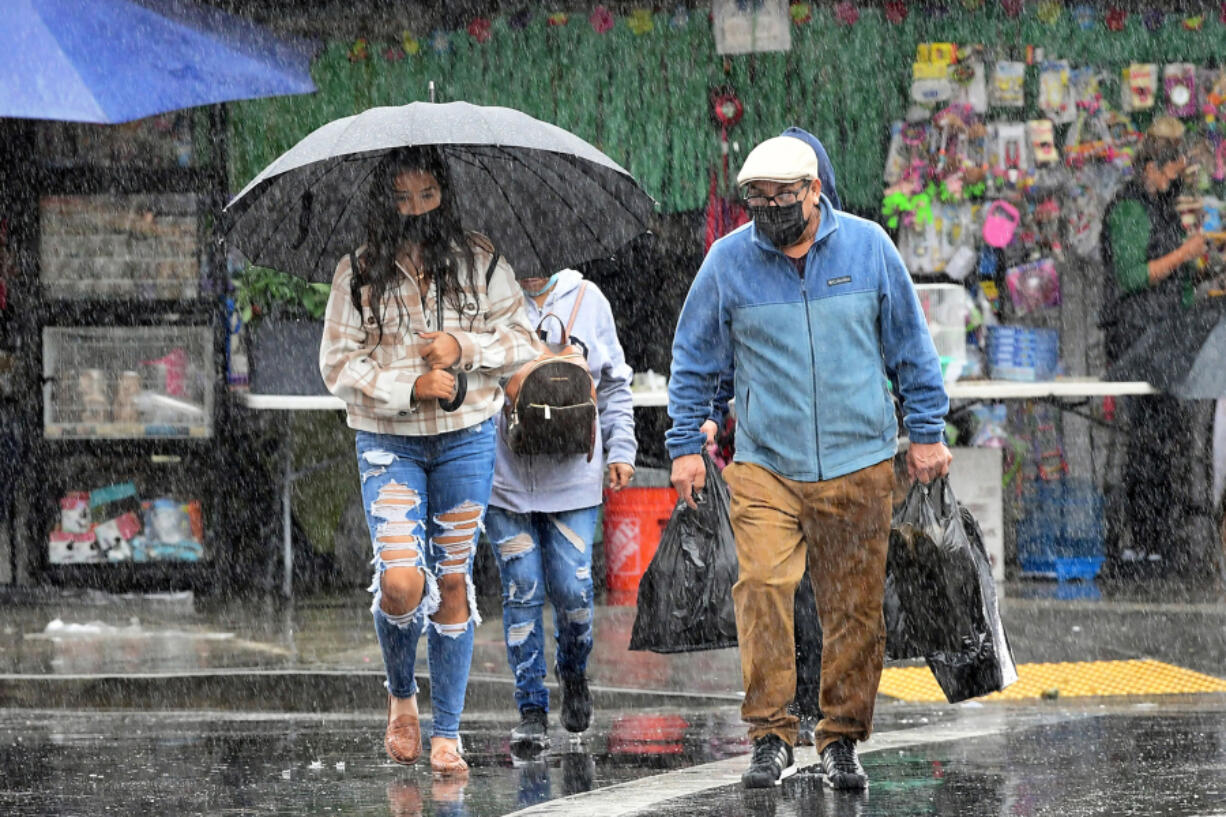 People cross a street under heavy rain in Los Angeles, California on Oct. 25, 2021. (Frederic J.