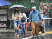 People cross a street under heavy rain in Los Angeles, California on Oct. 25, 2021. (Frederic J.