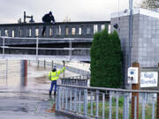 One worker stands on a closed bridge as another on the flooded walkway below where a flood wall at left holds back the Skagit River from downtown Mount Vernon, Wash., Tuesday, Nov. 16, 2021. An atmospheric river—a huge plume of moisture extending over the Pacific and into Washington and Oregon—caused heavy rainfall in recent days, bringing major flooding in the area.