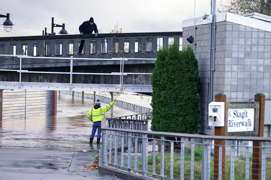 One worker stands on a closed bridge as another on the flooded walkway below where a flood wall at left holds back the Skagit River from downtown Mount Vernon, Wash., Tuesday, Nov. 16, 2021. An atmospheric river—a huge plume of moisture extending over the Pacific and into Washington and Oregon—caused heavy rainfall in recent days, bringing major flooding in the area.