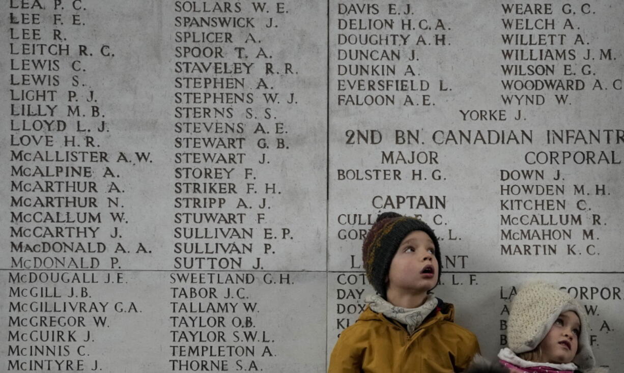 Two children look up at a wall of the missing during an Armistice Day ceremony at the Menin Gate Memorial to the Missing in Ypres, Belgium, Thursday, Nov. 11, 2021.