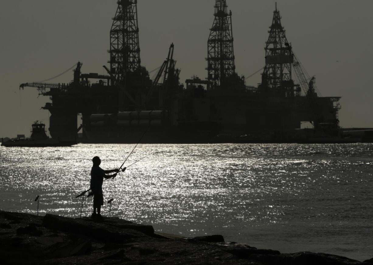 FILE - A man wears a face mark as he fishes near docked oil drilling platforms, Friday, May 8, 2020, in Port Aransas, Texas. The U.S. Interior Department on Wednesday, Nov. 17, 2021, is auctioning vast oil reserves in the Gulf of Mexico estimated to hold up to 1.1 billion barrels of crude. It's the first such sale under President Joe Biden and underscores the challenges he faces to reach climate goals that rely on cuts in fossil fuel emissions.