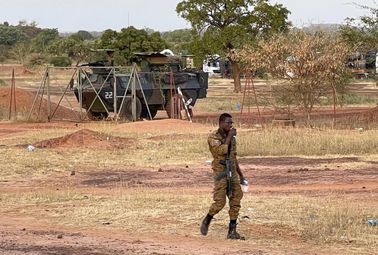 A Burkinabe soldier walks past a French Armoured Personnel Carrier part of a French military convoy heading to Niger, stopped by protesters in Kaya, Burkina Faso, Saturday Nov. 20, 2021. Residents of the city have blocked the roads to protest about the lack of security, and are not allowing a French military convoy to continue.