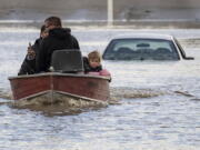 People, including a toddler and dog who were stranded by high water due to flooding are rescued by a volunteer operating a boat in Abbotsford, British Columbia, on Tuesday, Nov. 16, 2021.