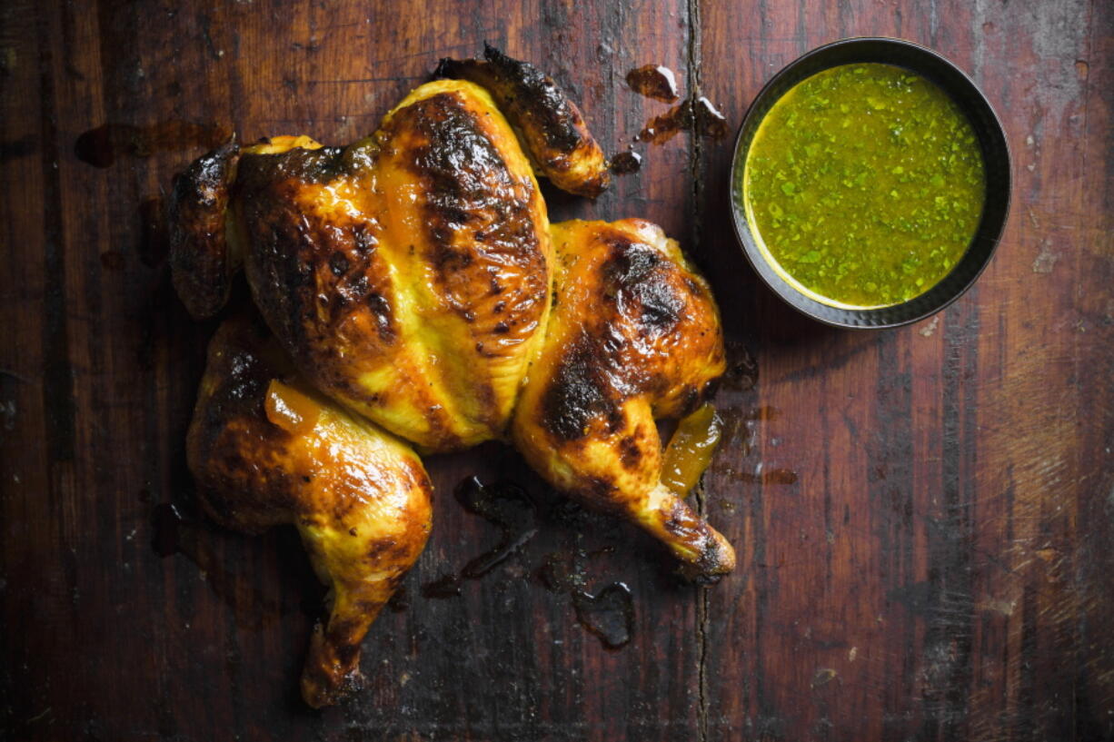 This image released by Milk Street shows a recipe for chutney-glazed spatchcocked chicken. Spatchcocking, or butterflying, involves cutting out a bird's backbone so it can be flattened. This allows the chicken to brown evenly and helps the glaze stay put. Their simple glaze mixes tangy-sweet chutney with butter and turmeric. Citrus juice added to a portion of the glaze before cooking makes a bright dipping sauce.