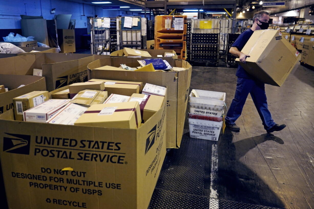 A worker carries a large parcel at the United States Postal Service sorting and processing facility, Thursday, Nov. 18, 2021, in Boston. Last year's holiday season was far from the most wonderful time of the year for the beleaguered U.S. Postal Service.