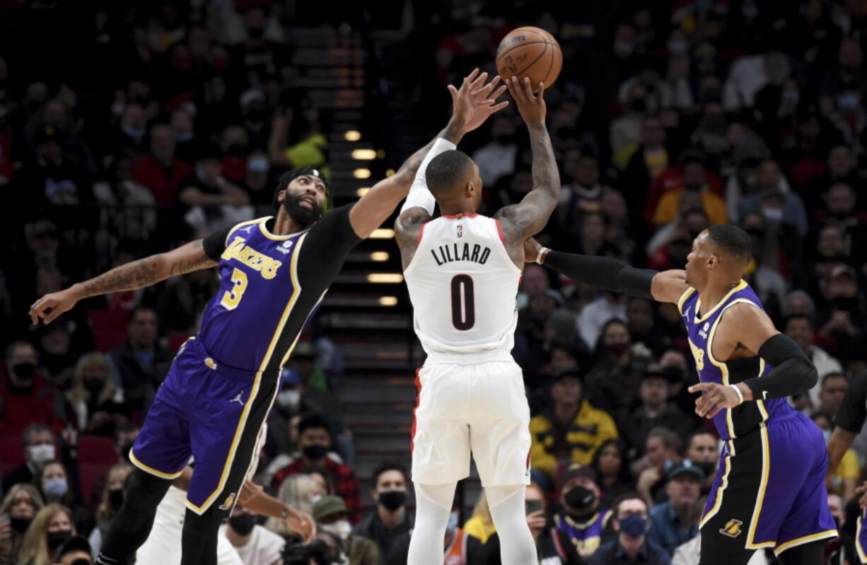 Portland Trail Blazers guard Damian Lillard, center, hits a 3-point shot from between Los Angeles Lakers Anthony Davis, left, and guard Russell Westbrook during the first half of an NBA basketball game in Portland, Ore., Saturday, Nov. 6, 2021.