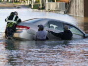 One man jumps on the back of car to try to keep the front from sinking further as others surround it, with the driver still aboard, that went into the flooded Nooksack River on Main Street, Tuesday, Nov. 16, 2021, in Ferndale, Wash. The group of citizens went into the river and stopped the car from floating further or sinking, whose driver had gone past a road closed sign, then muscled it back onshore. No one was injured.