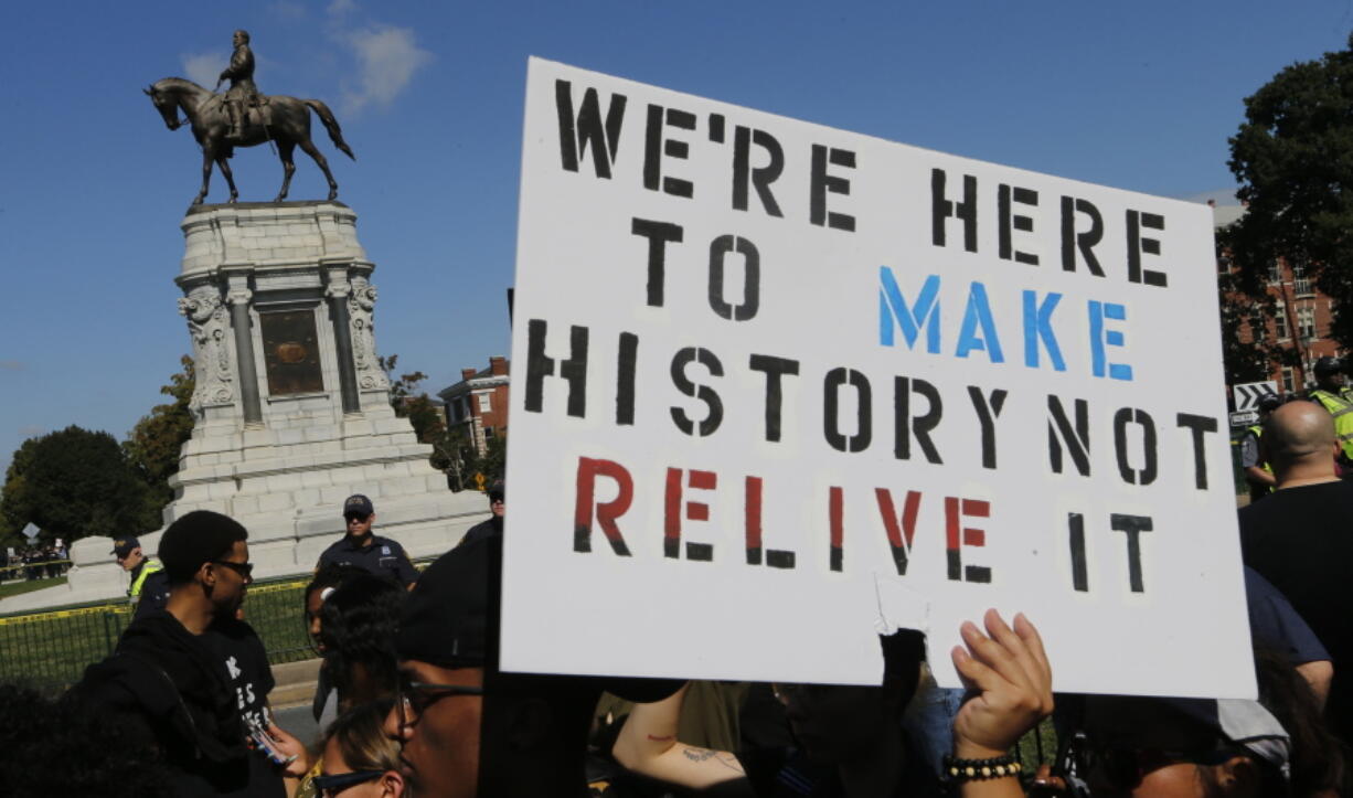 FILE - In this Saturday, Sept. 16, 2017 file photo, protesters hold signs in front of the statue of Confederate General Robert E. Lee on Monument Avenue in Richmond, Va.  A jury began deliberations Friday, Nov.