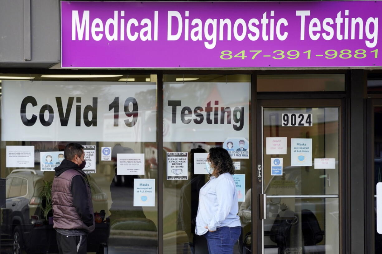 FILE - In this Oct. 21, 2020, file photo, an Exam Corp Lab employee, right, wears a mask as she talks with a patient lined up for COVID-19 testing in Niles, Ill.  Millions of U.S. workers now have a Jan. 4 deadline to get a COVID vaccine. The federal government on Thursday, Nov. 4, 2021 announced new vaccine requirements for workers at companies with more than 100 employees as well as workers at health care facilities that treat Medicare and Medicaid patients. (AP Photo/Nam Y.