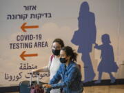 Travelers wearing protective face masks arrive at Ben Gurion Airport near Tel Aviv, Israel, Sunday, Nov. 28, 2021. Israel on Sunday approved barring entry to foreign nationals and the use of controversial technology for contact tracing as part of its efforts to clamp down on a new coronavirus variant.