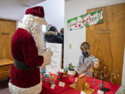 Santa Claus stops by the dinosaur-themed station run by fourth-grader Ezra LePage-Linch, 9, during the Lupine Holiday Market on Thursday afternoon. Students at Lupine Experiential School in Vancouver participated in a student-led market as a part of their economics curriculum.  At top, festive holiday rock magnets by seventh-grader Roman Ferguson, 13, are on display at the market.