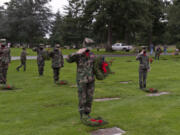 Young Marines Sgt. Gabriel Blok, 16, lays a wreath and salutes the grave of a veteran Saturday at Evergreen Memorial Gardens in Vancouver.  At top,  Lewis & Clark Young Marines practice folding the flag before the official ceremonies begin.