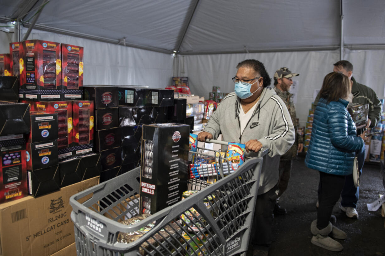 Brett Corpuz of Portland joins a crowd of shoppers as he picks up fireworks ahead of the New Year's holiday at Mean Gene Fireworks in Hazel Dell on Thursday afternoon. It has been about 18 months since vendors could sell fireworks. Although Clark County's interim ordinance is increasing business opportunities for firework stands, vendors are still struggling to make up for previous financial losses.