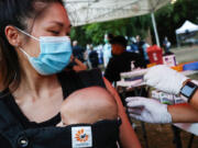 A person receives a COVID-19 vaccination dose, while carrying a baby in tow, as part of a National Night Out event hosted by Melrose Action on Aug. 3, 2021 in Los Angeles.