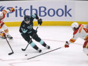 Seattle Kraken center Morgan Geekie, center, drives between Calgary Flames center Dillon Dube, left, and defenseman Rasmus Andersson during the first period of an NHL hockey game Thursday, Dec. 30, 2021, in Seattle. (AP Photo/Ted S.