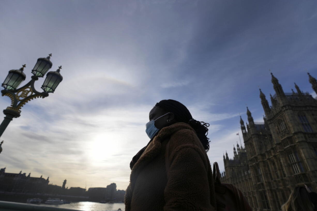 A woman wears a face covering as she crosses Westminster Bridge in London, Thursday, Dec. 9, 2021. British Prime Minister Boris Johnson has announced tighter restrictions to stem the spread of the omicron variant. He is again urging people to work from home and mandating COVID-19 passes to get into nightclubs and large events.