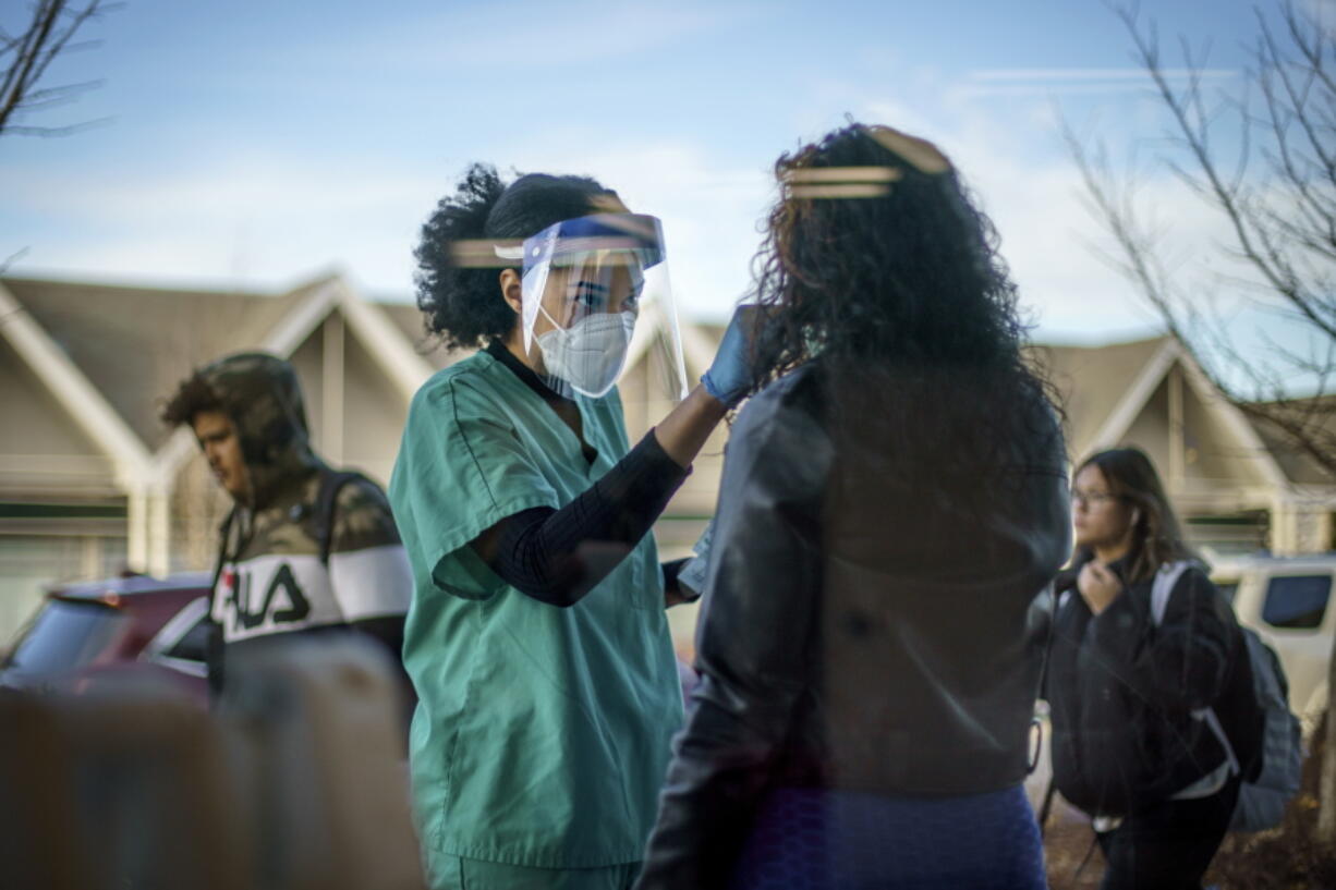 FILE - Maya Goode, a COVID-19 technician, performs a test on Jessica Sanchez outside Asthenis Pharmacy in Providence, R.I., Dec. 7, 2021. As the omicron variant sparks worldwide fears of renewed virus outbreaks, Americans' worries about infection are again on the rise. But fewer say that they are regularly wearing masks or isolating compared with the beginning of the year.