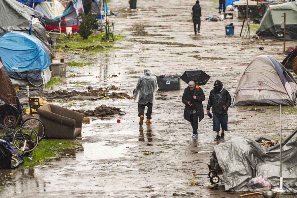 People walk through a partially flooded homeless encampment at Riverwalk Park in Santa Cruz, Calif., Monday, Dec. 13, 2021. A major storm hitting Northern California is expected to intensify and bring travel headaches and a threat of localized flooding after an abnormally warm fall in the U.S. West.