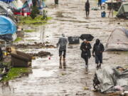 People walk through a partially flooded homeless encampment at Riverwalk Park in Santa Cruz, Calif., Monday, Dec. 13, 2021. A major storm hitting Northern California is expected to intensify and bring travel headaches and a threat of localized flooding after an abnormally warm fall in the U.S. West.