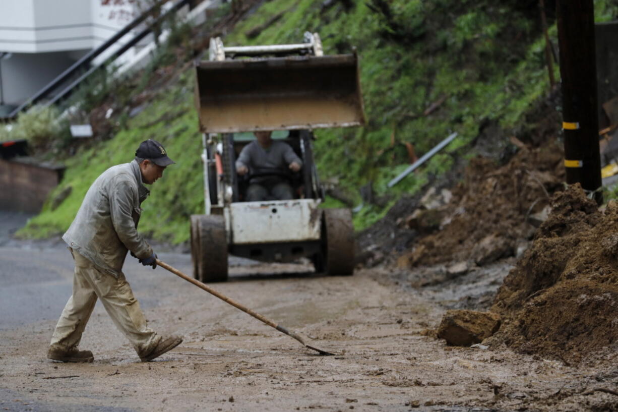 Workers clear a mudslide from a double lot on Westover Drive in Oakland, Calif., on Thursday, Dec. 23, 2021. Heavy overnight rains in Northern California left two people dead in a submerged car as authorities on Thursday urged residents of several Southern California mountain and canyon communities to voluntarily leave their homes because of possible mud and debris flows.