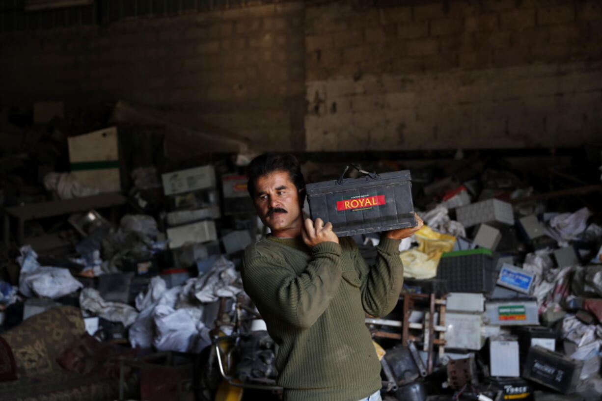 A Palestinian worker carries a discarded battery at a warehouse in Jebaliya, Gaza Strip, Wednesday, Dec. 15, 2021. In a territory suffering from chronic power outages, batteries are needed to keep most Gaza households running. But huge mounds of used batteries are piling up at makeshift outdoor landfills, posing a threat to public health and the environment.