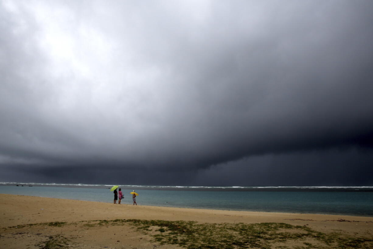 People hold umbrellas as it begins to rain on an otherwise empty beach in Honolulu on Monday, Dec. 6, 2021. A strong storm packing high winds and extremely heavy rain flooded roads and downed power lines and tree branches across Hawaii, with officials warning Monday of potentially worse conditions ahead.