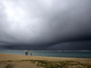 People hold umbrellas as it begins to rain on an otherwise empty beach in Honolulu on Monday, Dec. 6, 2021. A strong storm packing high winds and extremely heavy rain flooded roads and downed power lines and tree branches across Hawaii, with officials warning Monday of potentially worse conditions ahead.