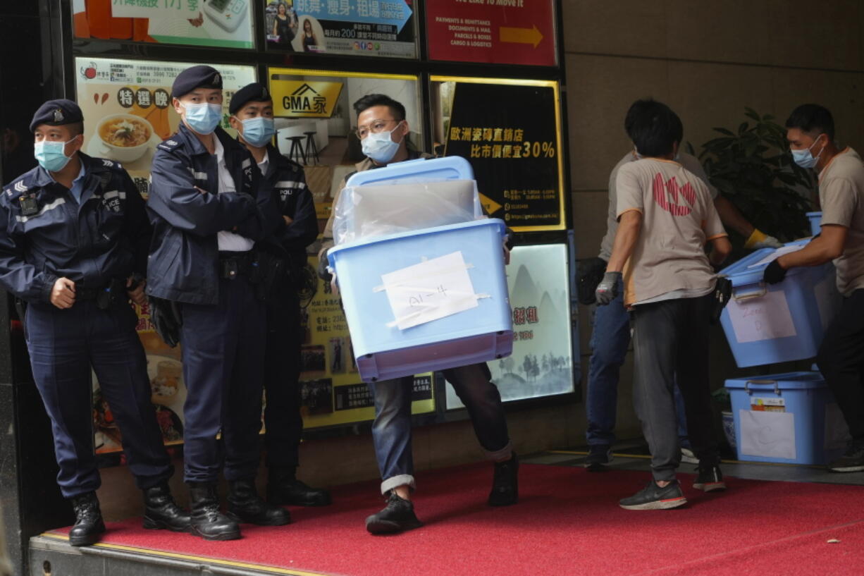 Workers carry some evidences walks past police officers outside office of "Stand News" in Hong Kong Wednesday, Dec. 29, 2021. Hong Kong police raided the office of the online news outlet on Wednesday after arresting several people for conspiracy to publish a seditious publication.